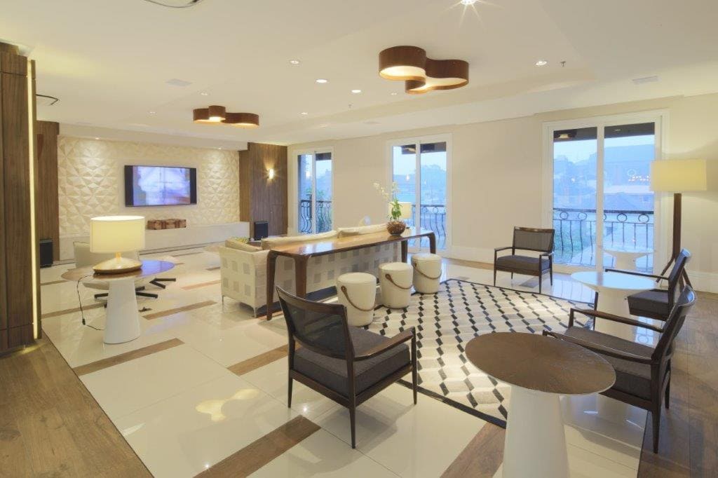 Sala de estar moderna com sofás brancos, poltronas, mesa redonda e grandes janelas com vista para a água.