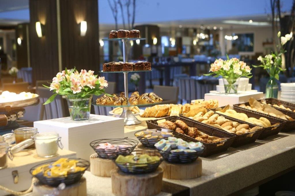 Elegante mesa de buffet com doces, flores e sobremesas empratadas em um ambiente de jantar com iluminação suave.