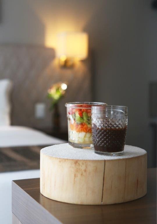 Duas bebidas em uma bandeja redonda de madeira sobre uma mesa em um quarto com iluminação suave.
