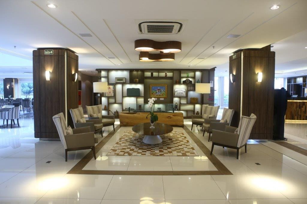 Área de estar moderna no lobby do hotel, com sofás, poltronas, mesa de centro e iluminação aconchegante.