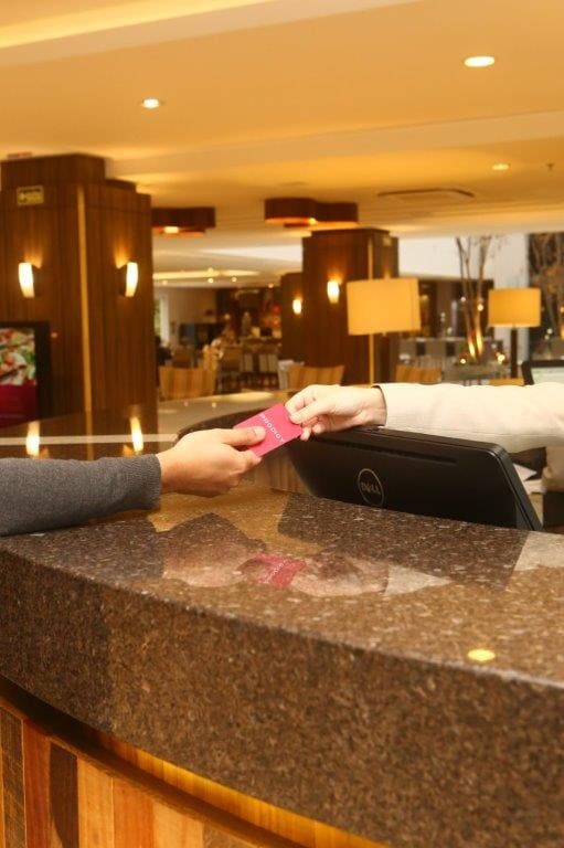 Entregando um cartão rosa na recepção do hotel, em um saguão com iluminação aconchegante.