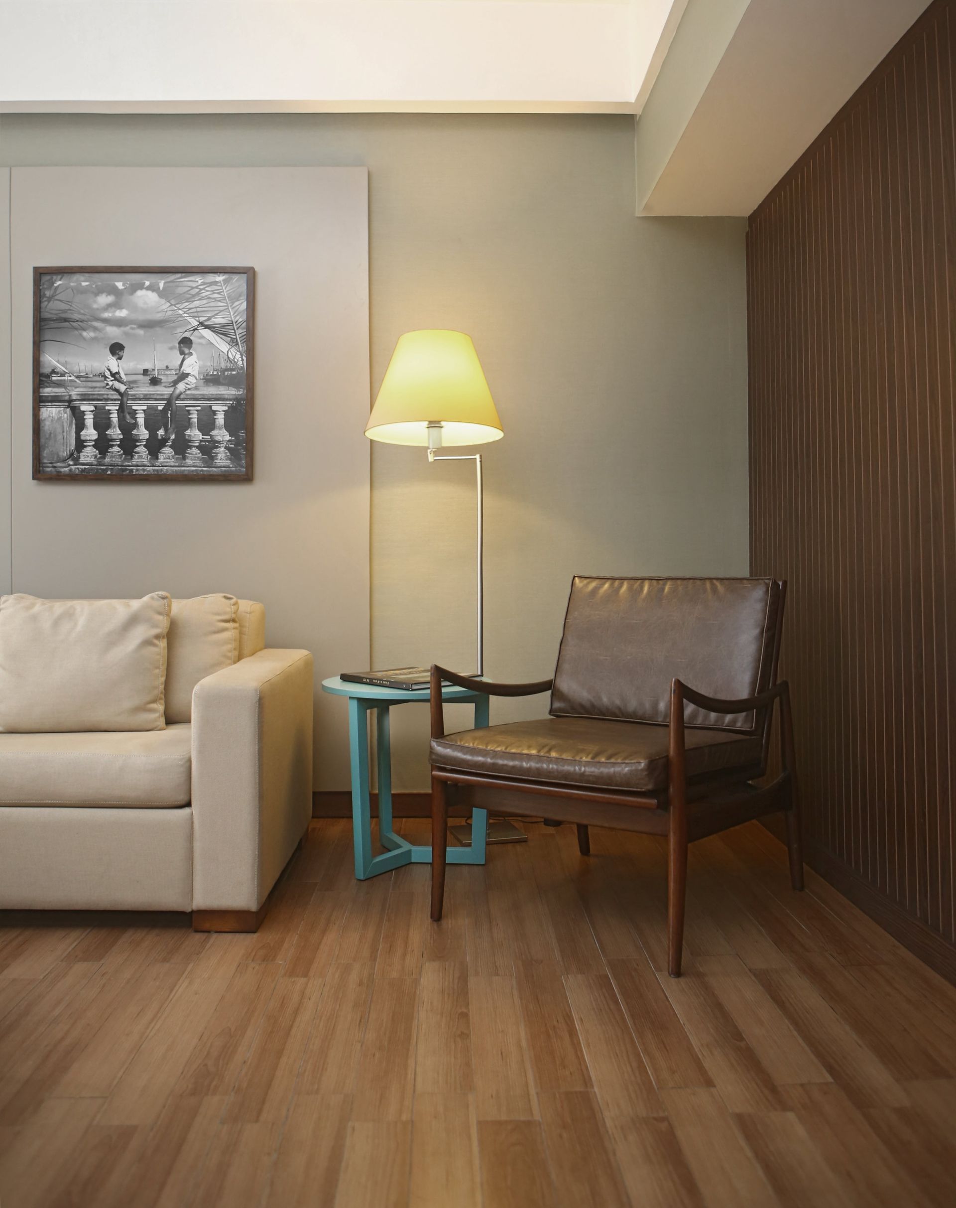 Sala de estar moderna com sofá bege, luminária, mesinha de centro, cadeira de madeira e parede com painéis de madeira sobre piso de madeira.