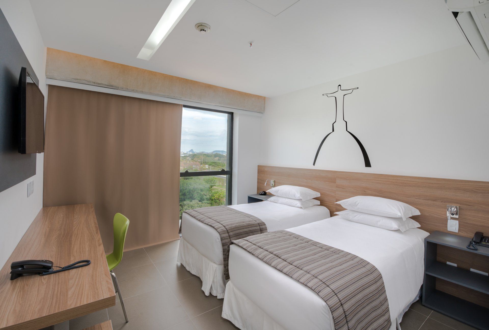 Quarto de hotel moderno com duas camas de solteiro, uma escrivaninha, TV e uma grande janela com cortinas.