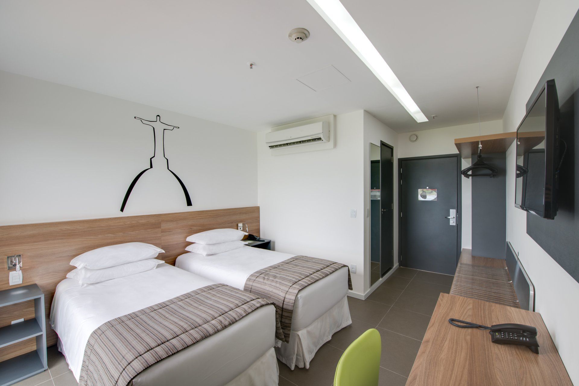 Quarto de hotel moderno com duas camas de solteiro, escrivaninha de madeira, TV de parede e decoração minimalista.