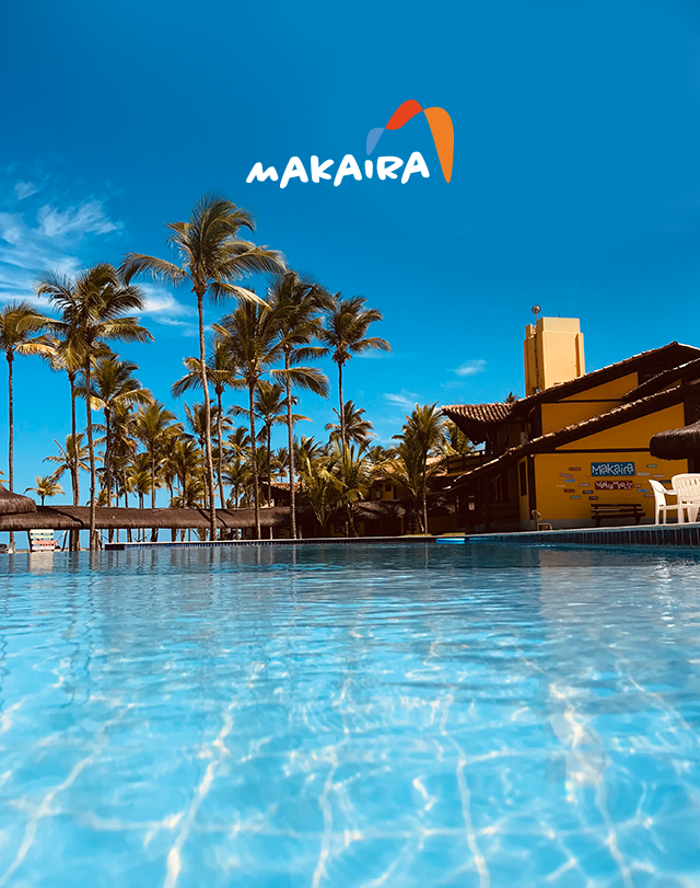 Resort à beira da piscina com palmeiras, água azul cristalina e um céu azul brilhante sob a placa Makaira.