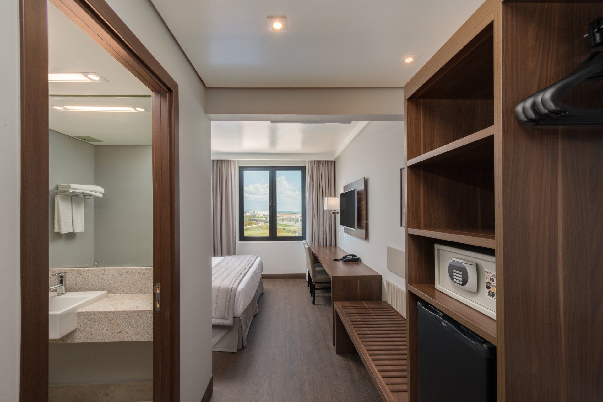 Quarto de hotel moderno com duas camas de solteiro, TV, prateleiras embutidas e porta aberta para o banheiro.