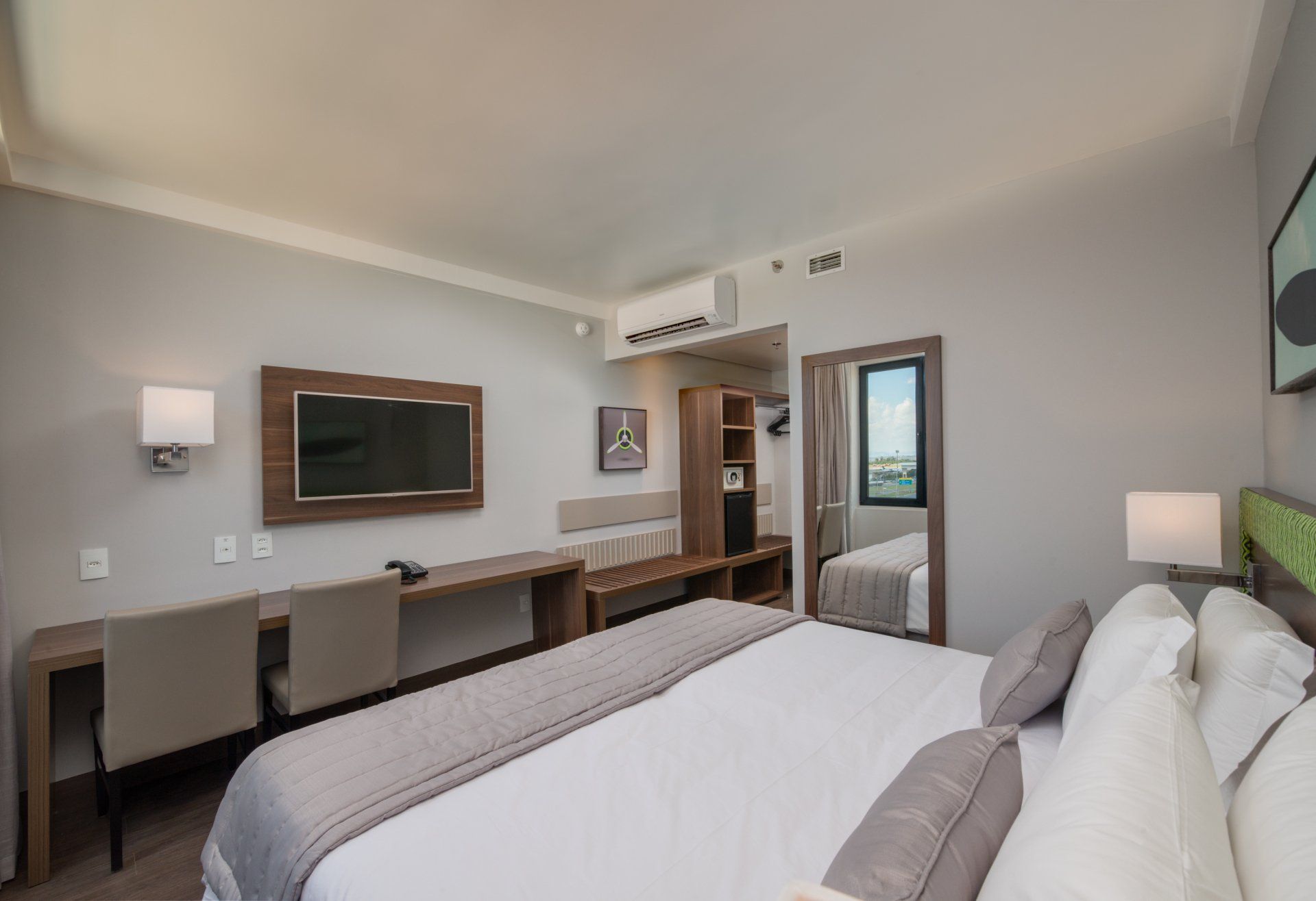 Quarto de hotel moderno com cama, escrivaninha, espelho de parede e porta para varanda.