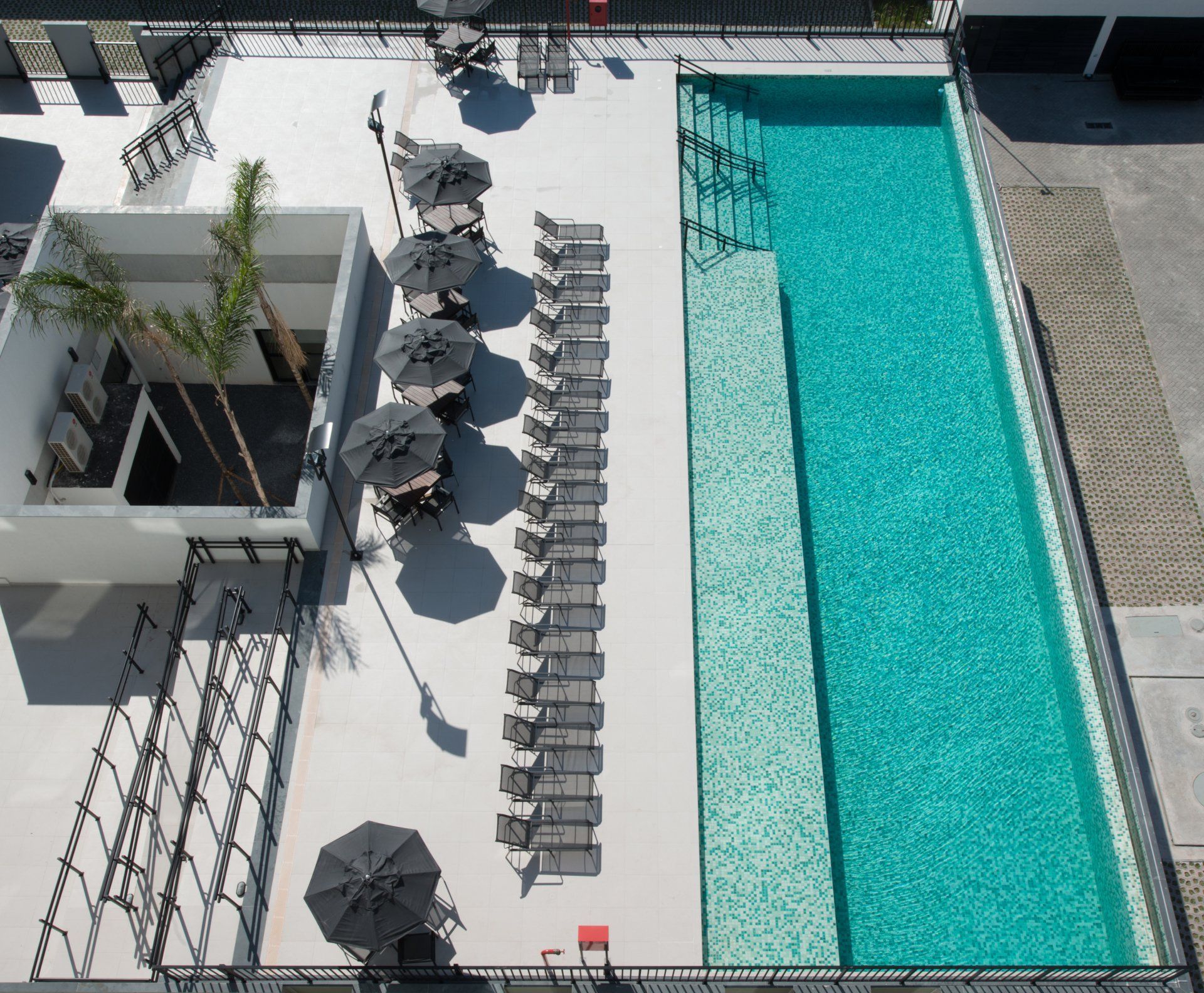 Vista aérea de uma piscina na cobertura com espreguiçadeiras e guarda-sóis cinzentos ao lado de água turquesa.