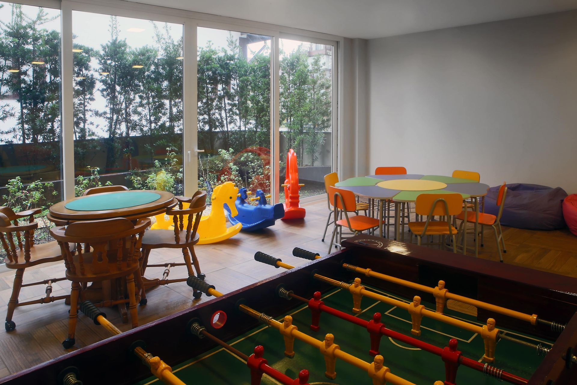 Sala de jogos iluminada com pebolim, mesas de brinquedos e brinquedos coloridos para montar perto de grandes janelas.