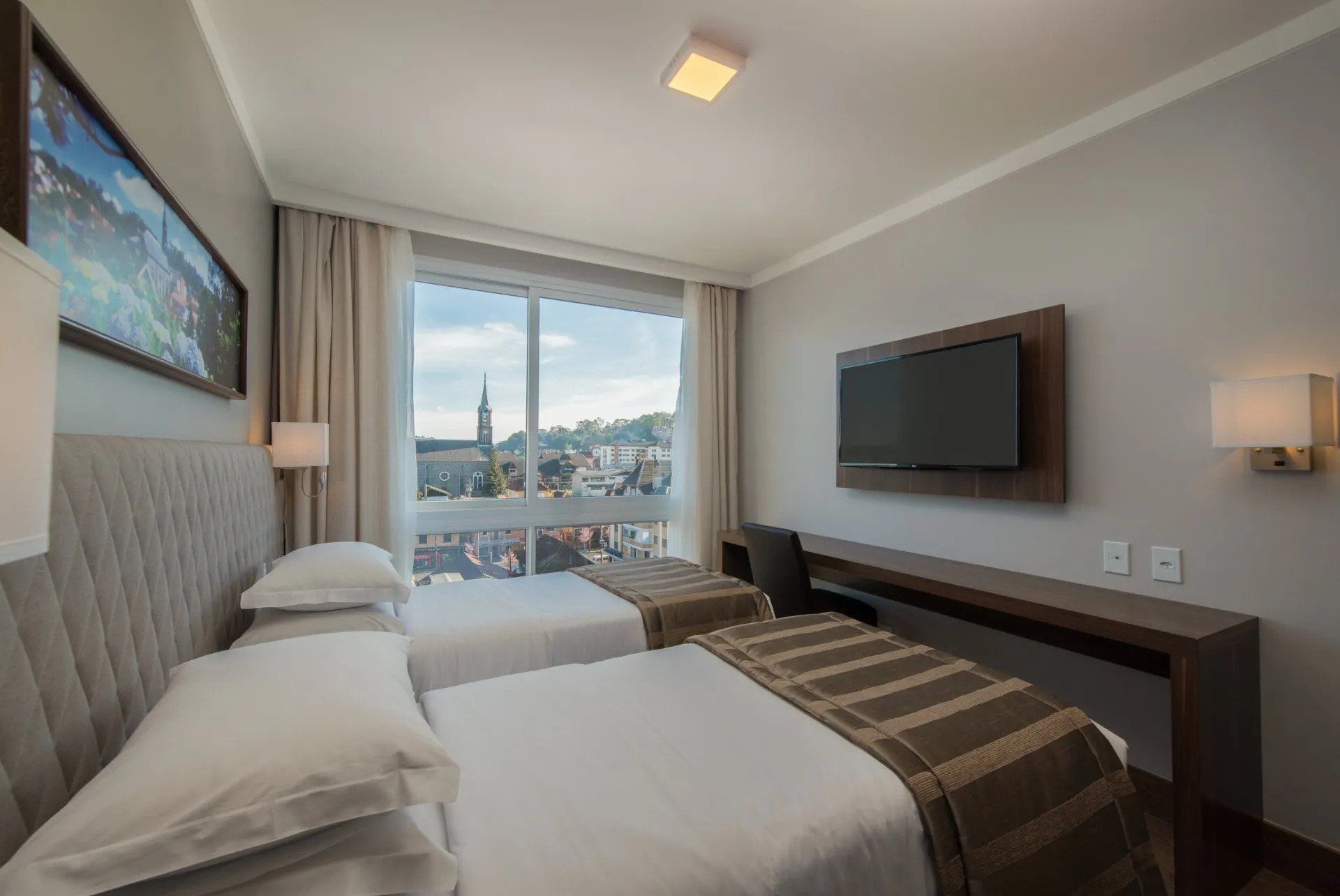 Quarto de hotel moderno com duas camas de solteiro, TV de parede e janela ampla com vista para o horizonte da cidade.