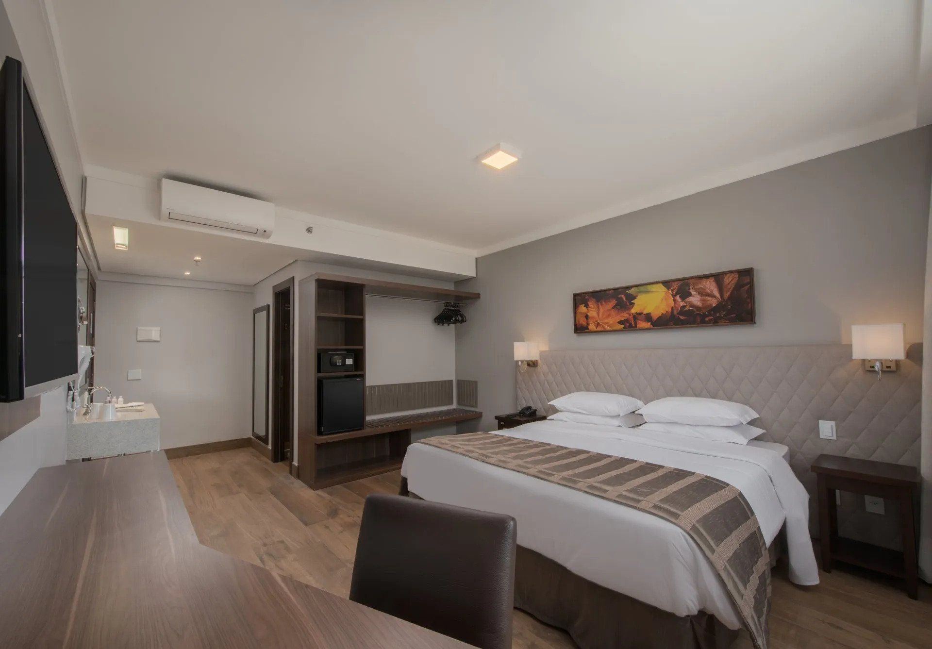 Quarto de hotel moderno com cama, escrivaninha, guarda-roupa e obras de arte na parede em tons de cinza.