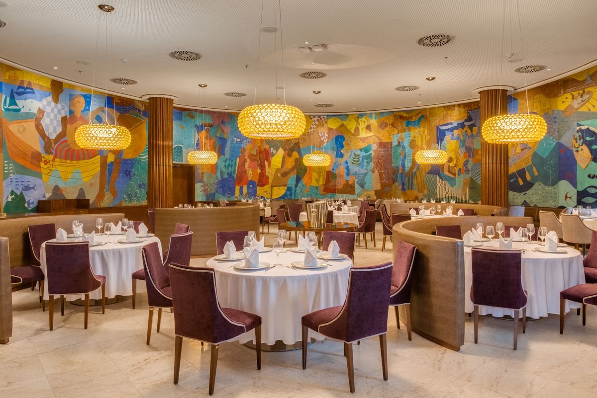 Sala de jantar elegante de restaurante com cadeiras roxas, toalhas de mesa brancas e um mural colorido na parede.