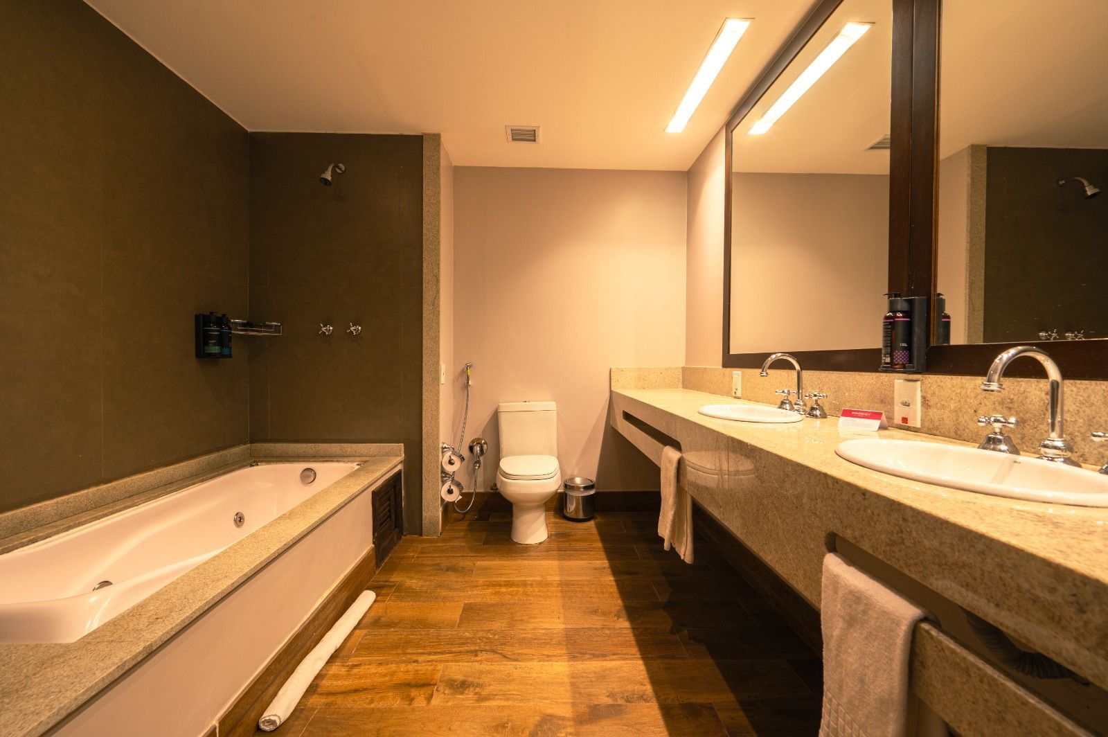 Banheiro de hotel moderno com pia dupla, espelho grande, banheira e vaso sanitário.
