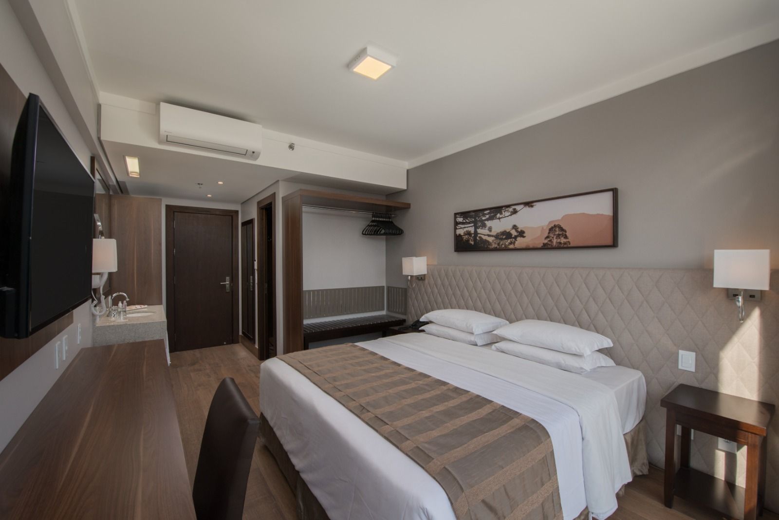 Quarto de hotel moderno com duas camas de solteiro, TV de parede, escrivaninha e decoração em tons de cinza.