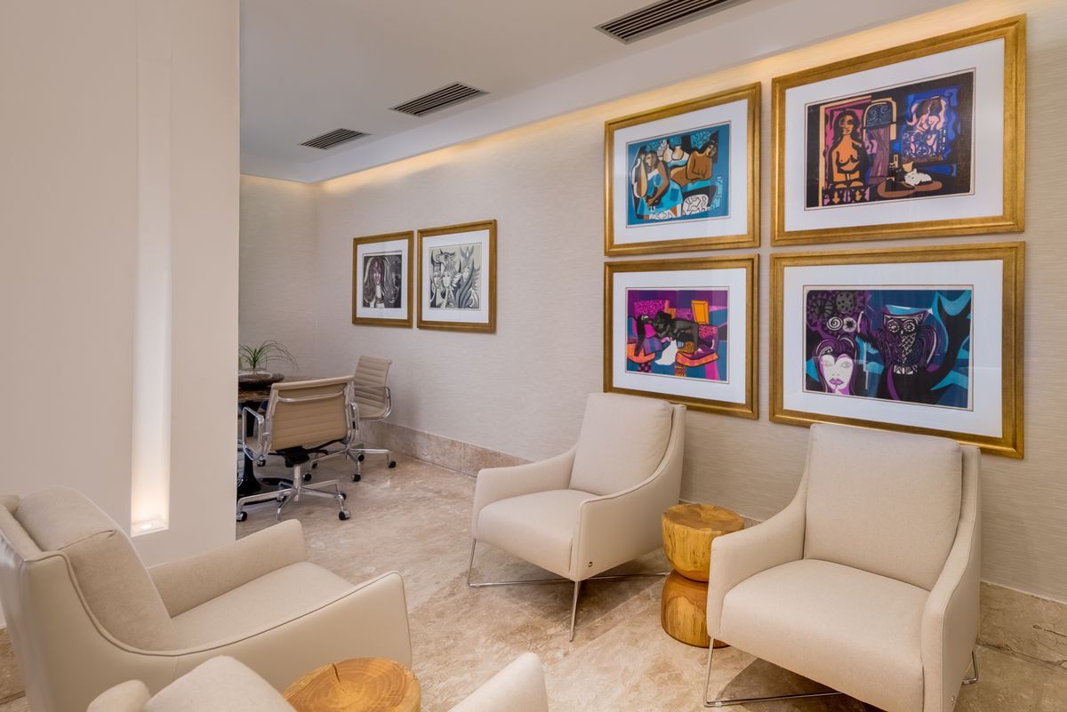 Sala de estar moderna com cadeiras bege e obras de arte coloridas emolduradas em uma parede de galeria.