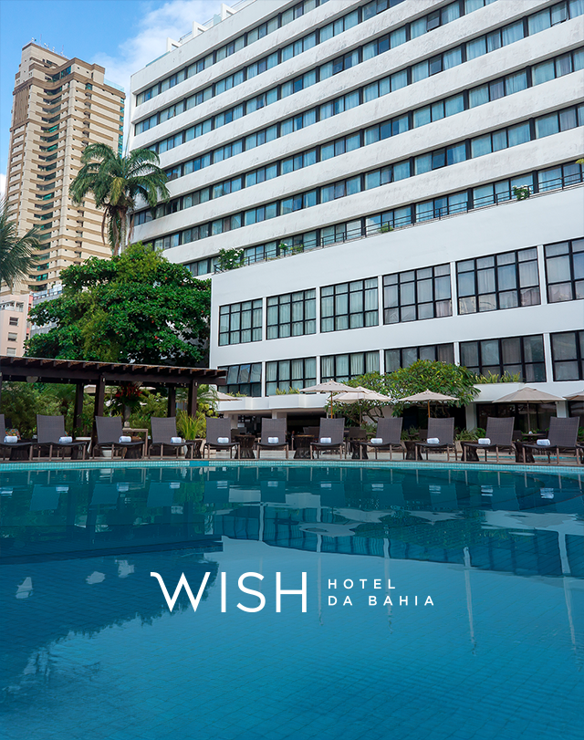 O Wish Hotel da Bahia fica ao lado de uma piscina azul, com um moderno arranha-céu branco e palmeiras.