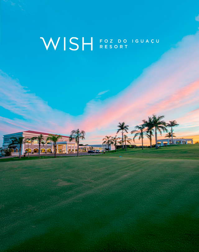 O WISH Foz do Iguaçu Resort ao pôr do sol, com gramado verde, palmeiras e céu rosa-azulado.