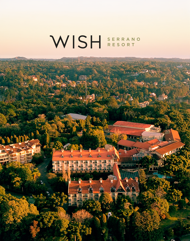 Vista aérea do Wish Serrano Resort em meio à densa floresta verde ao pôr do sol.