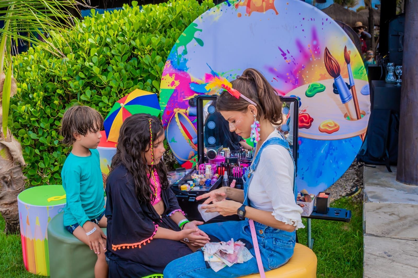 Quatro crianças com fantasias listradas segurando bolos decorados em um cenário de festa colorido.