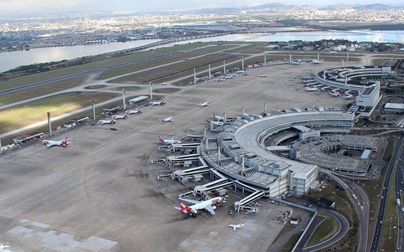 Vista aérea de um movimentado terminal aeroportuário com aviões estacionados nos portões de embarque e pistas ao lado da água.