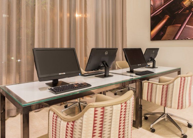 Estações de trabalho modernas com três monitores e cadeiras listradas em uma sala com cortinas.