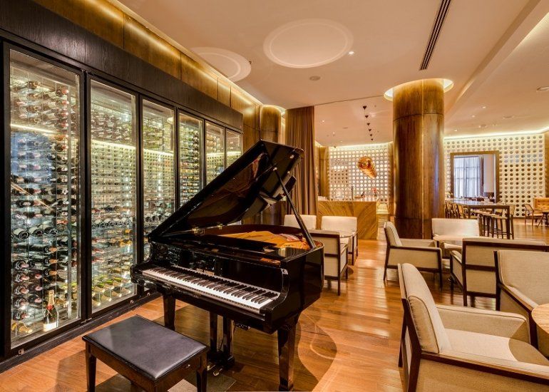 Piano de cauda em um lounge luxuoso com vista para a cidade, piso de madeira aconchegante e cadeiras cor creme.