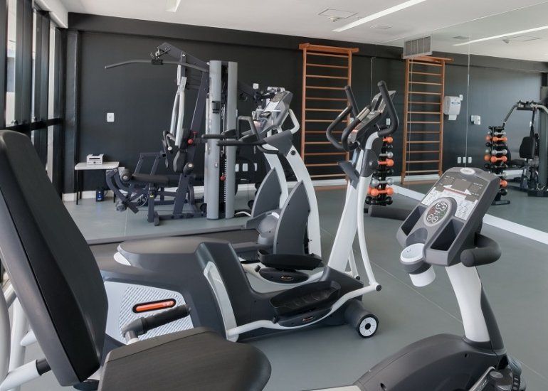 Academia moderna com aparelhos de cardio, equipamentos de musculação e barras de parede em uma sala cinza escura.