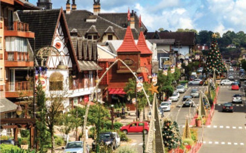 Rua movimentada em uma cidade pitoresca com prédios coloridos, carros estacionados e um semáforo vermelho.