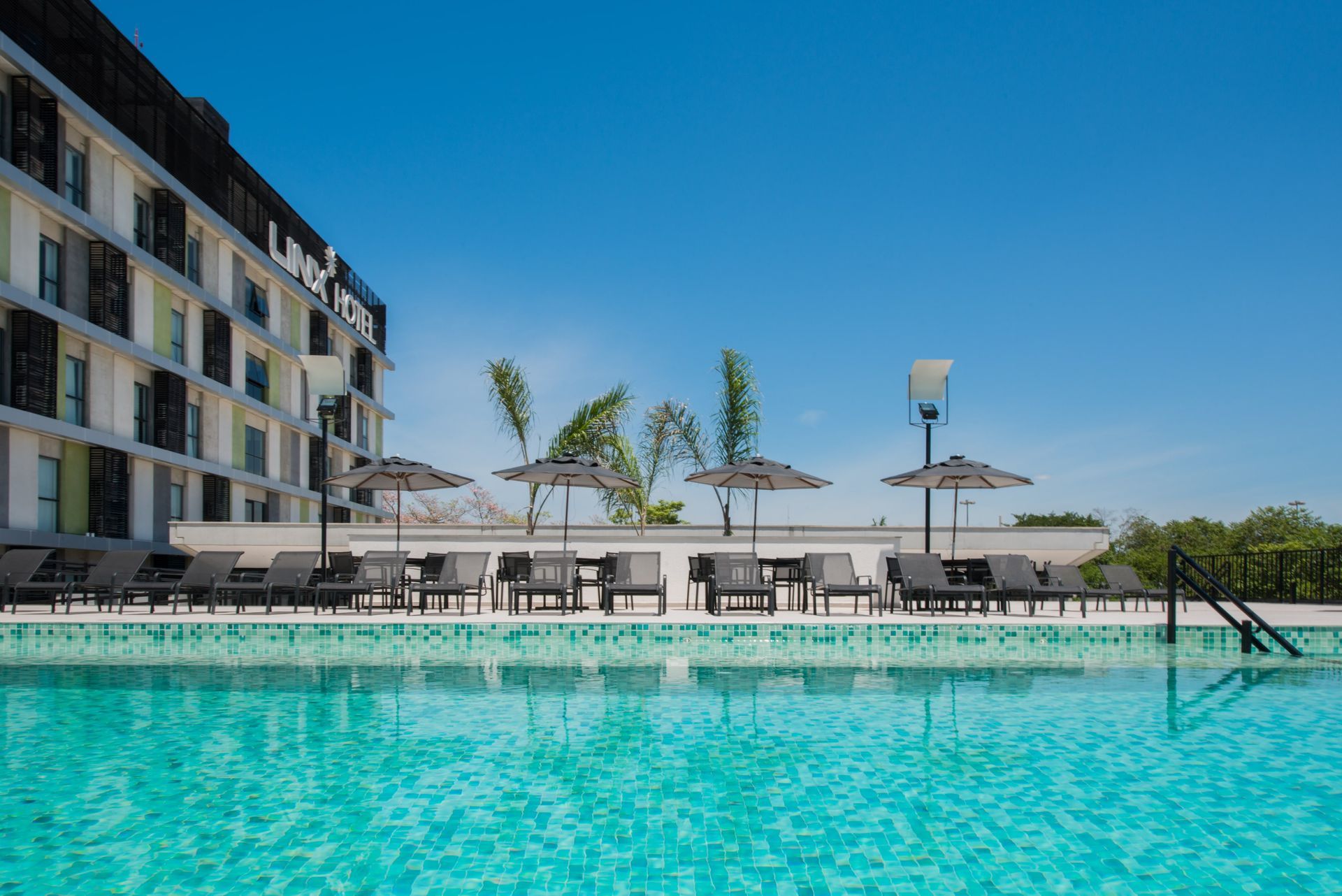 Piscina moderna em um apartamento com água turquesa, espreguiçadeiras, guarda-sóis e céu azul.