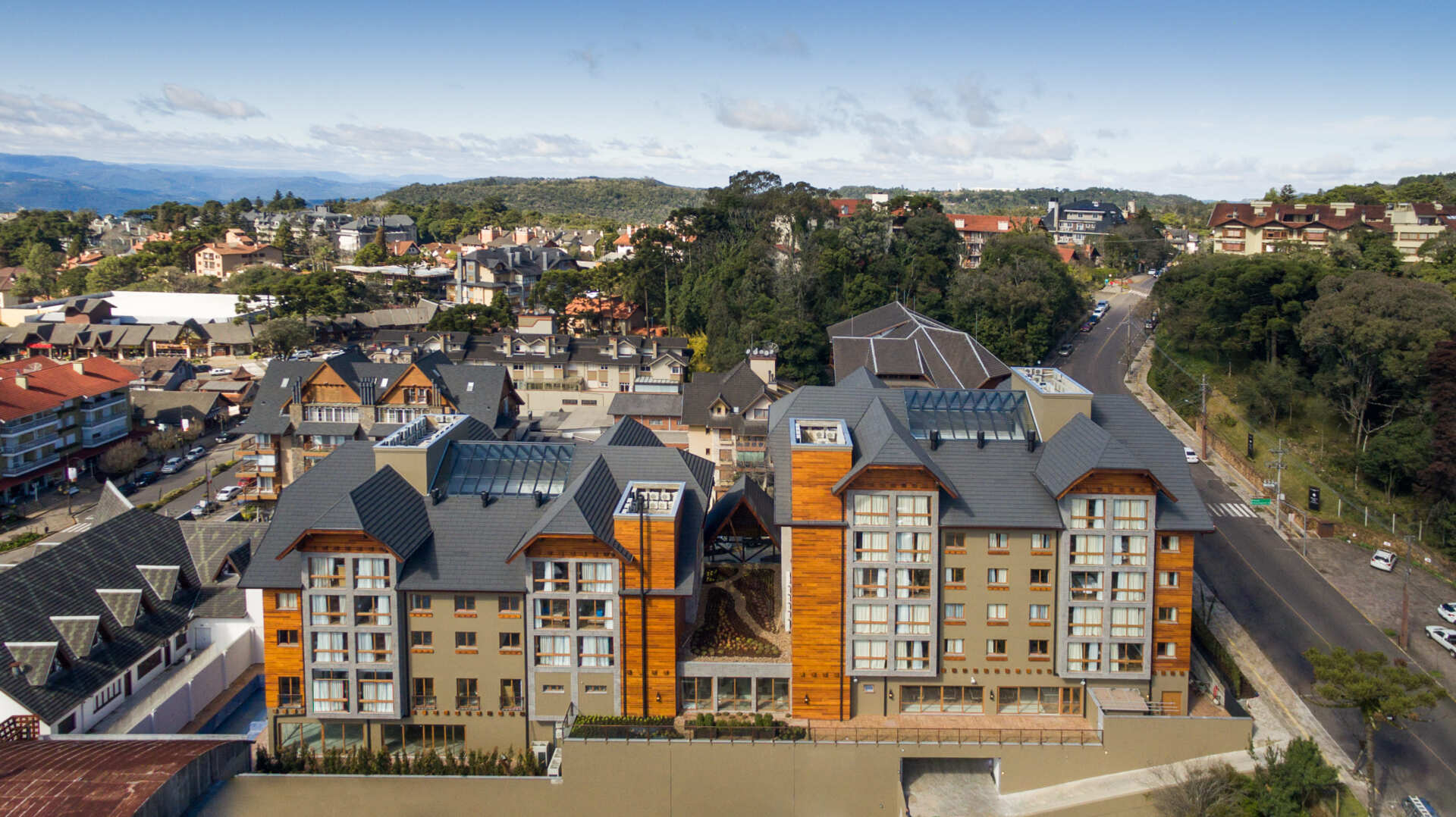 Vista aérea de prédios de apartamentos modernos ao lado de uma estrada e árvores em um bairro residencial.