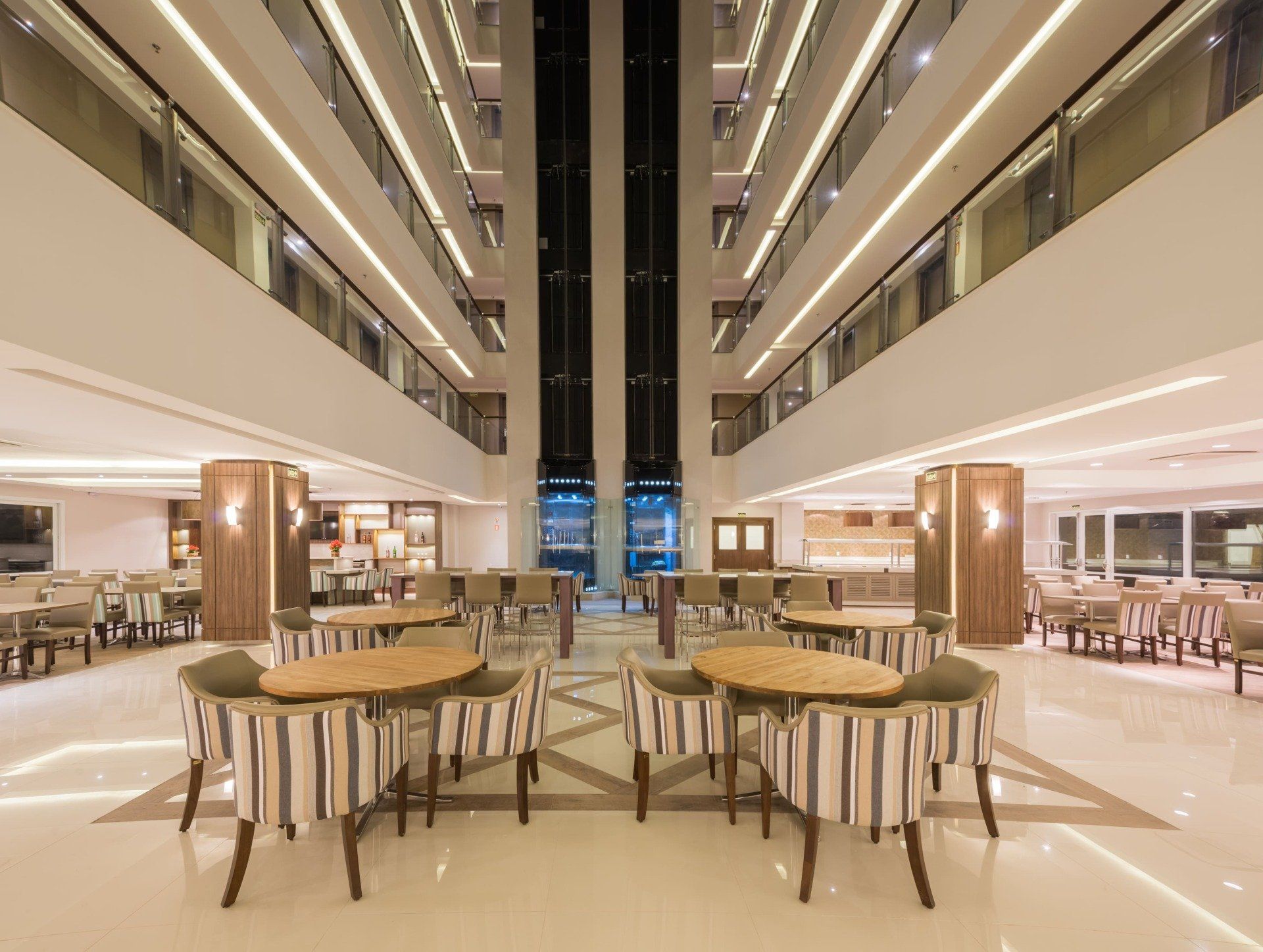Átrio moderno de hotel com área de estar, iluminação aconchegante e varandas de vários andares.