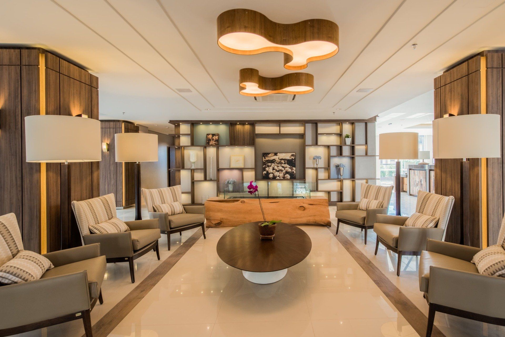 Sala de estar moderna com poltronas bege, mesa brilhante e iluminação pendente aconchegante em um interior simétrico.