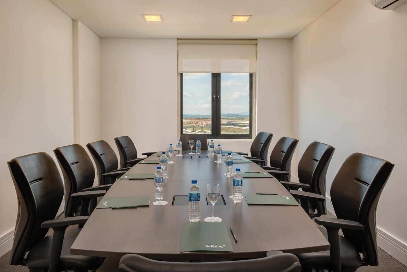 Sala de conferências com uma mesa comprida, cadeiras pretas e uma janela com vista para a cidade.