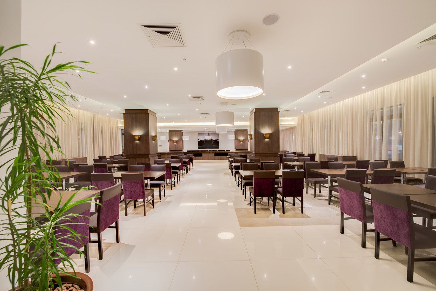 Restaurante de hotel elegante com cadeiras roxas, piso de mármore branco e iluminação suave de lustres.