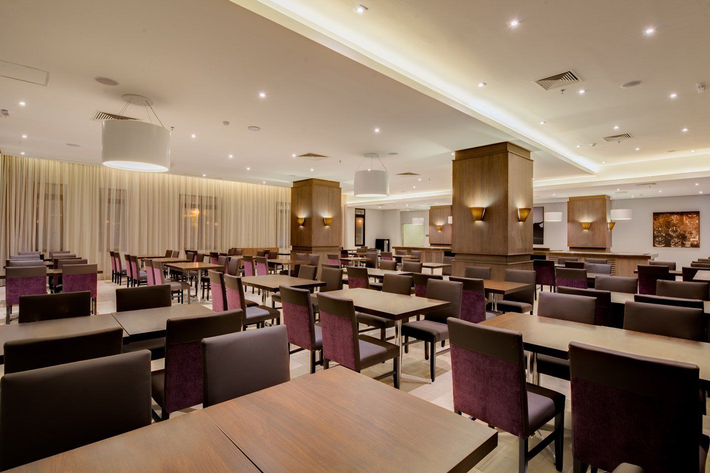 Sala de jantar moderna de hotel com mesas e cadeiras dispostas de forma organizada, iluminação aconchegante e detalhes em roxo.