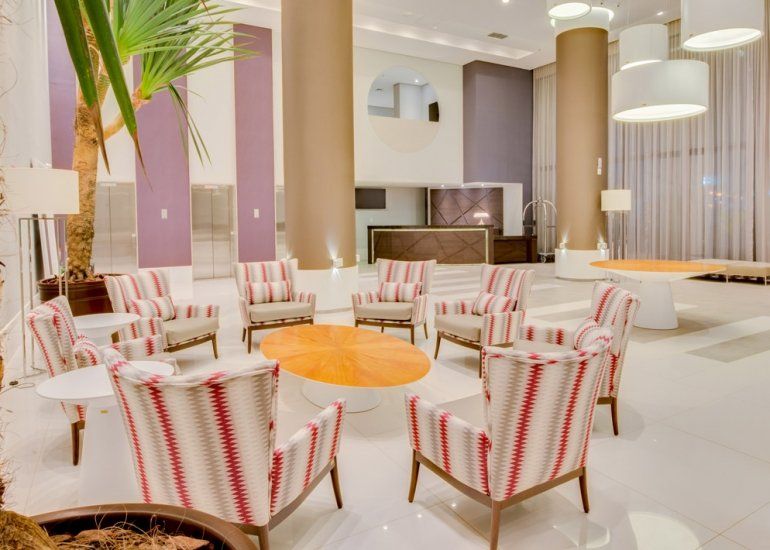 Sala de estar moderna de hotel com cadeiras listradas, mesa redonda laranja e luminárias pendentes.