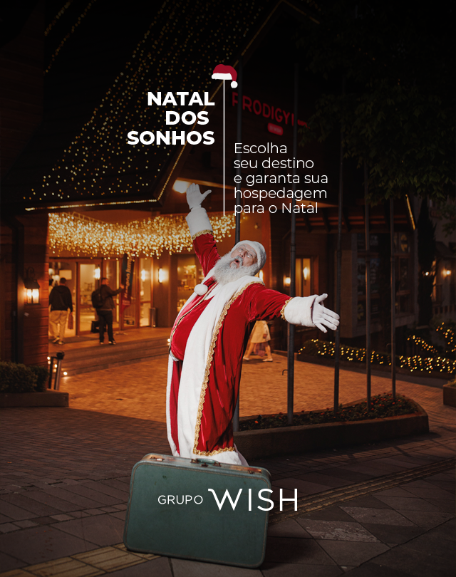 Papai Noel ao lado de caixa verde “Grupo Wish” em rua natalina iluminada à noite.