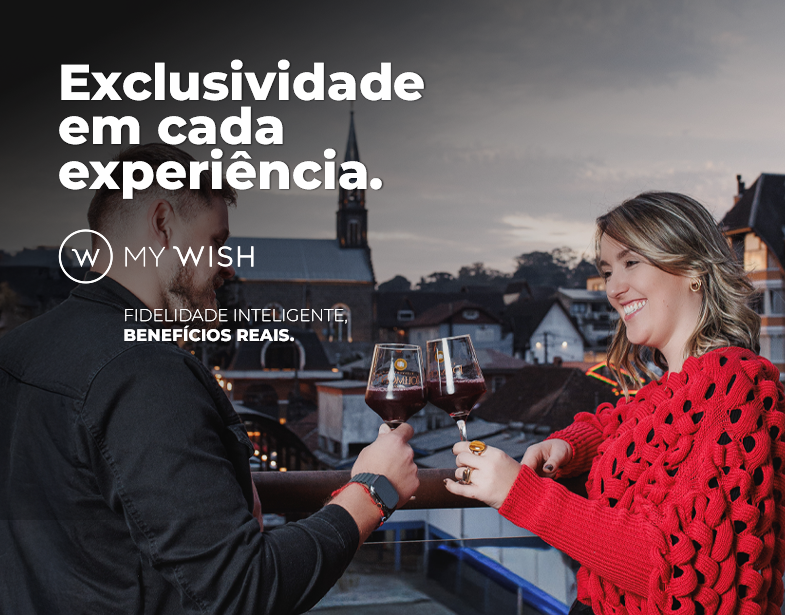 Casal brindando taças de vinho em um terraço ao pôr do sol, com texto publicitário “Exclusividade em cada experiência”.