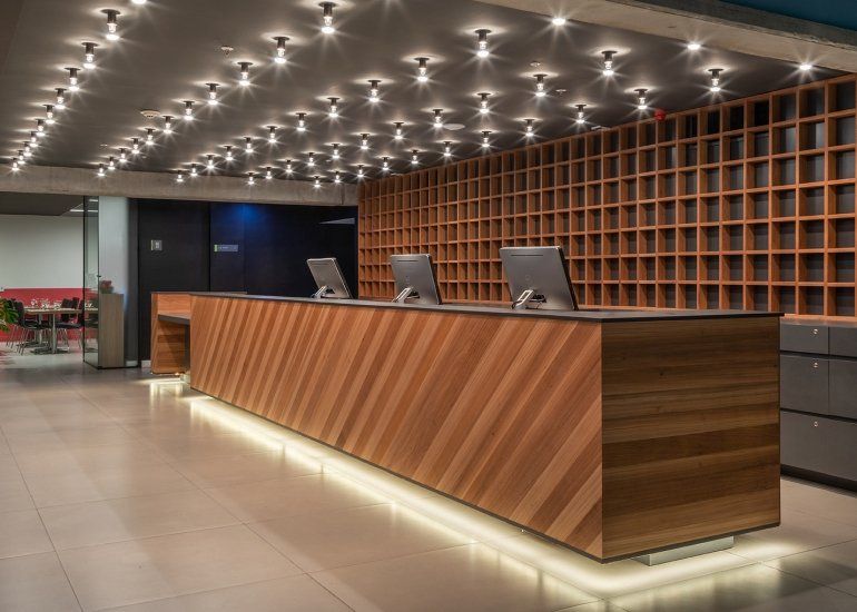Balcão de recepção de hotel moderno com painéis de madeira em tons quentes, luminárias pendentes e nichos vazios.