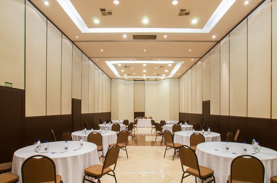 Salão de banquetes com mesas redondas, cadeiras e iluminação aconchegante no teto, preparado para um evento.