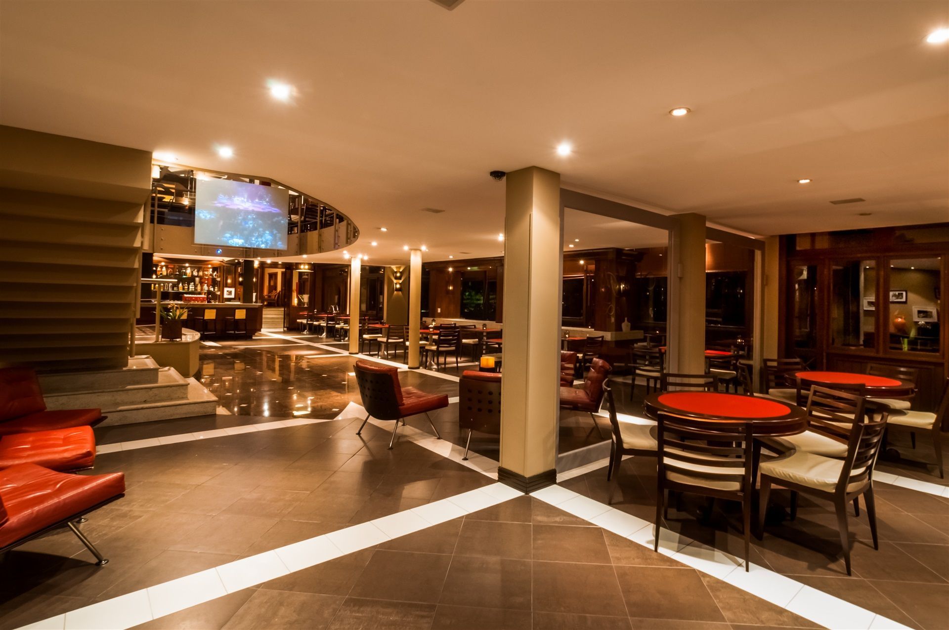 Interior de lounge moderno com assentos, mesas e área de bar na cor laranja ao entardecer.