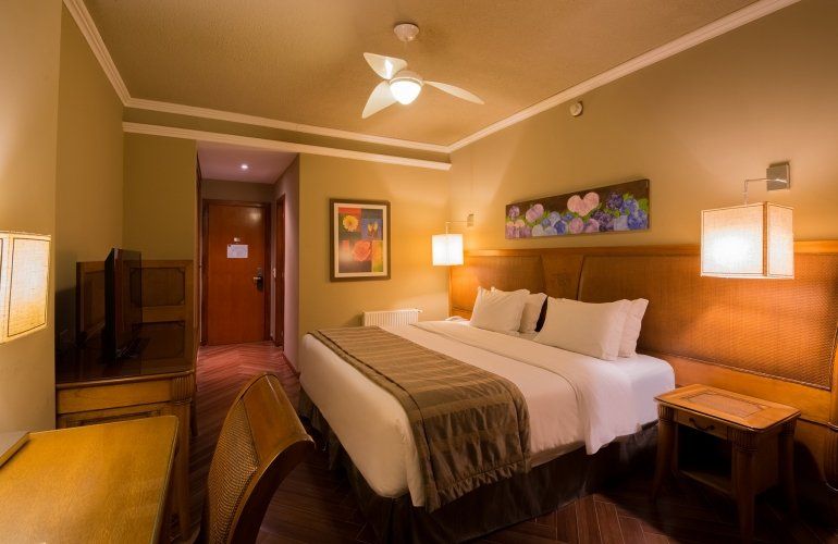 Quarto de hotel aconchegante com cama king-size, móveis de madeira, TV, luminárias e obras de arte emolduradas.