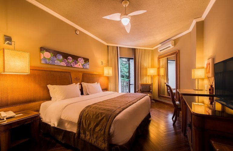 Quarto de hotel aconchegante com cama king-size, iluminação suave, escrivaninha e porta para a varanda.