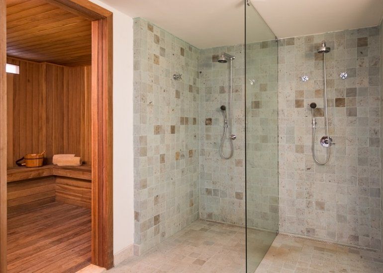 Banheiro de spa com box de vidro ao lado de uma sauna de madeira.