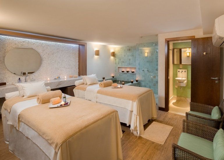 Quarto de hotel estilo spa com duas camas de solteiro, iluminação aconchegante e um pequeno banheiro visível através de uma porta aberta.