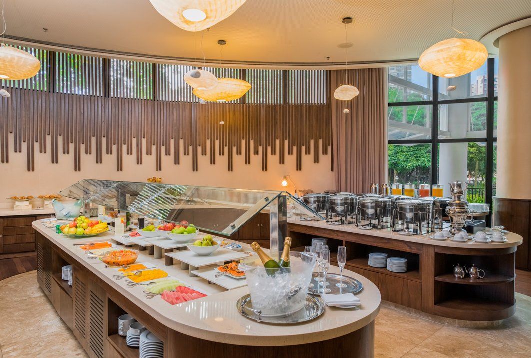 Sala de jantar tipo bufê com estações de comida redondas, utensílios de mesa e iluminação pendente aconchegante.