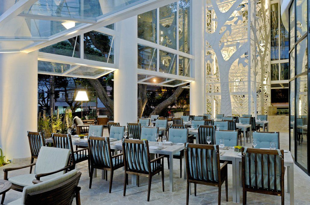 Restaurante luminoso e moderno com vigas brancas, janelas amplas e mesas e cadeiras bem arrumadas.