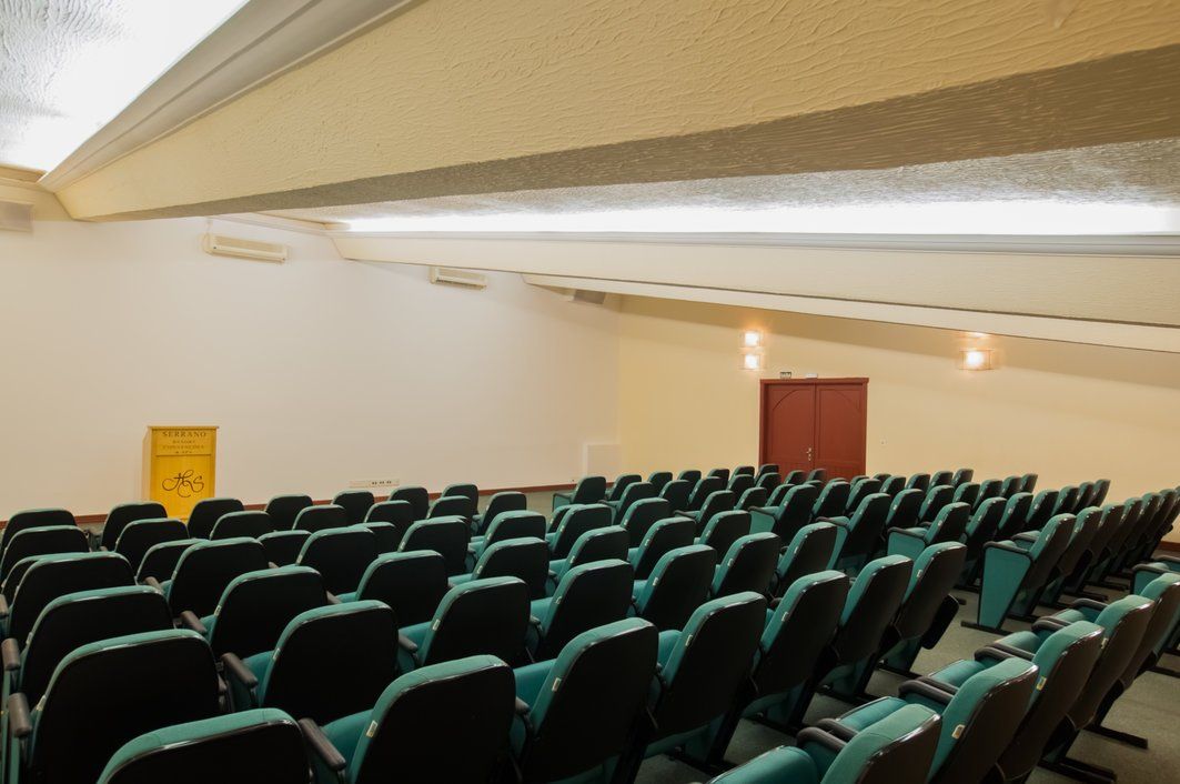 Auditório vazio com fileiras de assentos verdes e um palco na frente.
