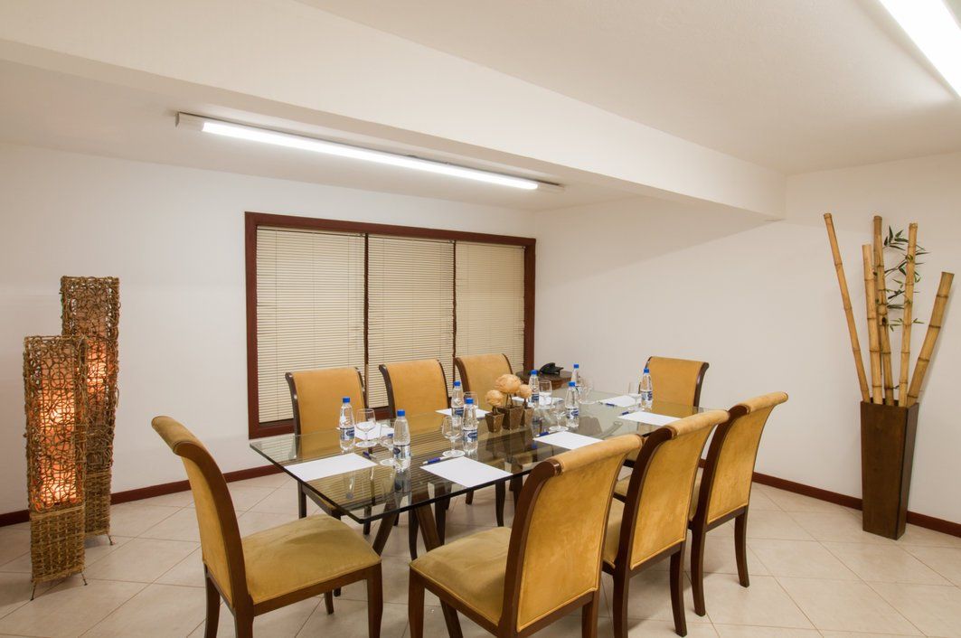 Sala de jantar elegante com mesa de vidro, cadeiras bege e detalhes decorativos em bambu.