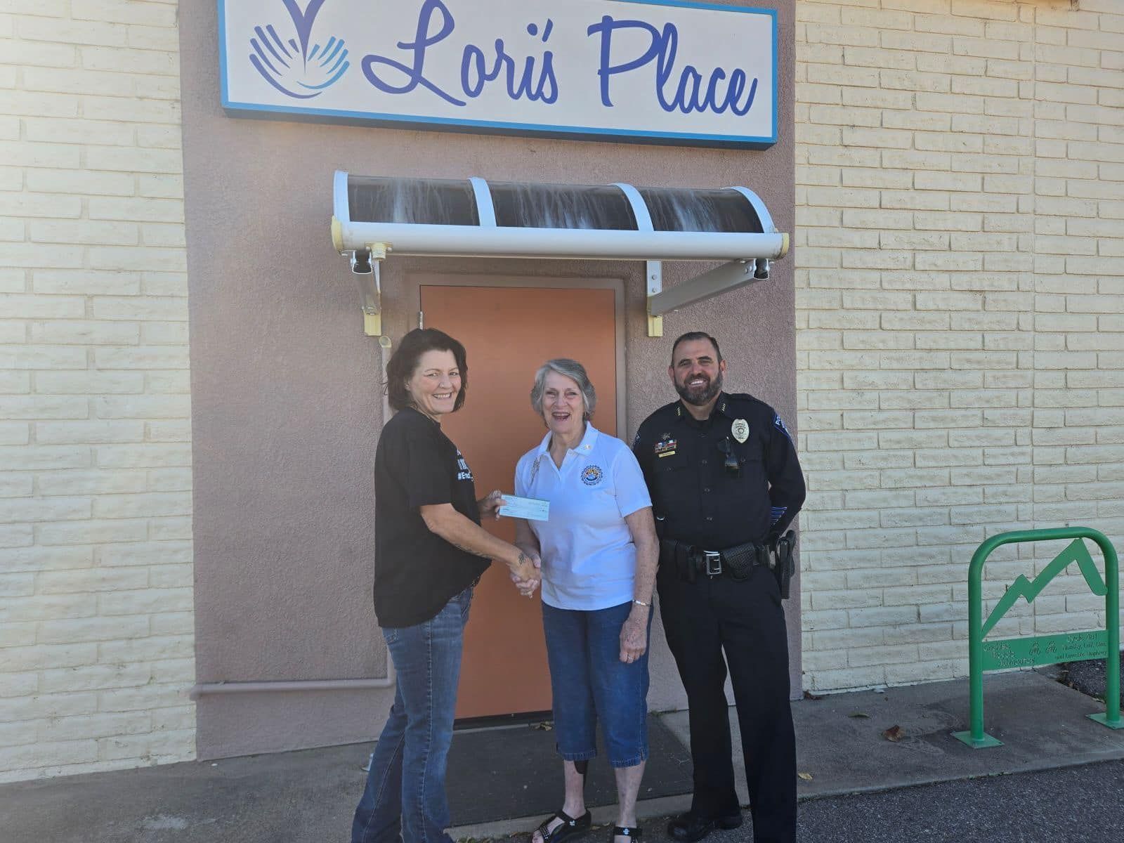 A woman is handing a check to a police officer in front of a loris place building.